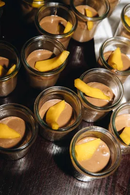 lots of little glasses filled with a chocolate dessert accompanied by cake and mango slices